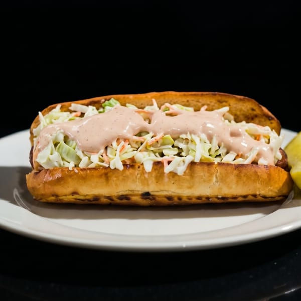 A hot dog bun filled with coleslaw and pink sauce, served with a lime wedge.