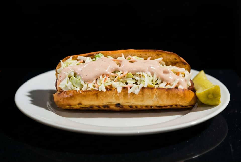 A hot dog bun filled with coleslaw and pink sauce, served with a lime wedge.