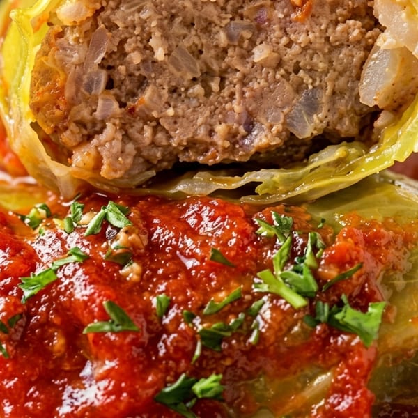 Close-up of a plate of cabbage rolls, one cut open to show the meat and rice filling.