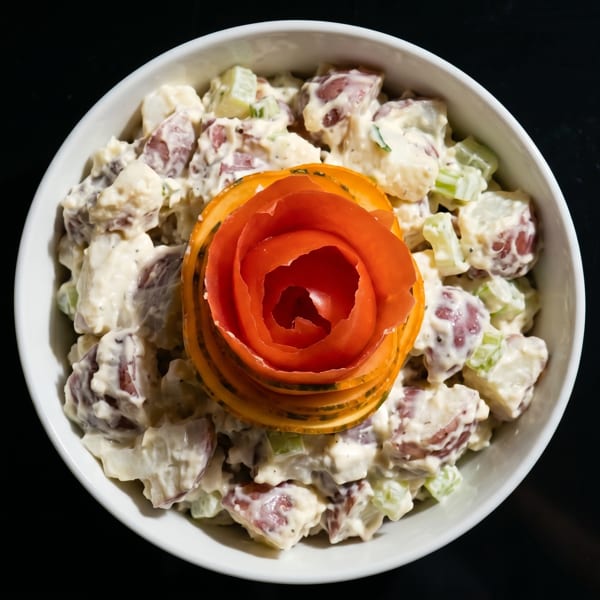 Creamy potato salad with red potatoes and celery, garnished with a carved tomato rose.