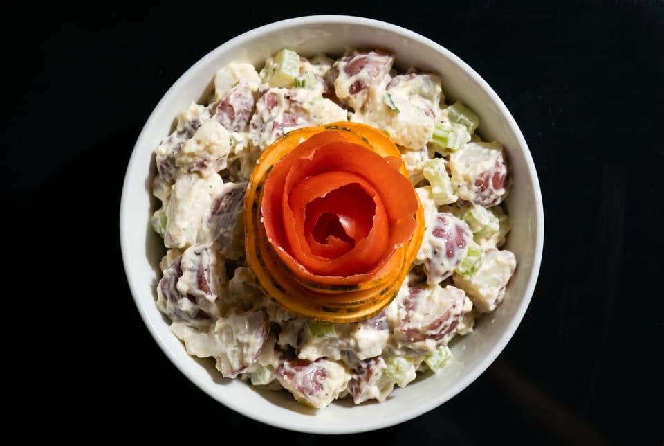 Creamy potato salad with red potatoes and celery, garnished with a carved tomato rose.