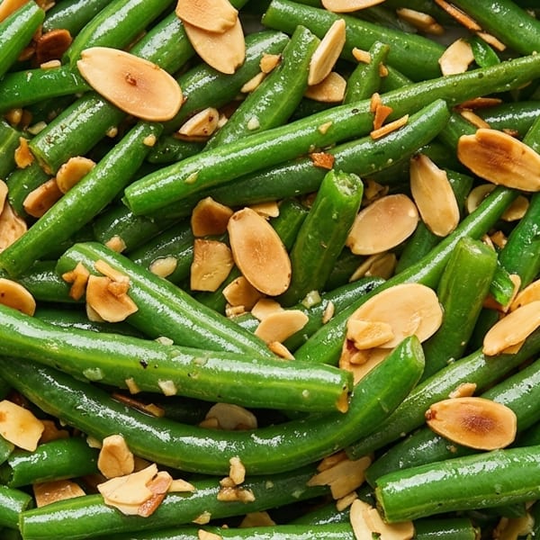 Close-up of vibrant green beans tossed with toasted almond slivers and seasonings on a white plate.