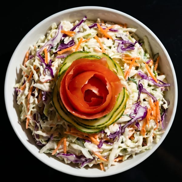 Coleslaw with shredded cabbage, carrots, and purple cabbage, garnished with a tomato and cucumber rose.