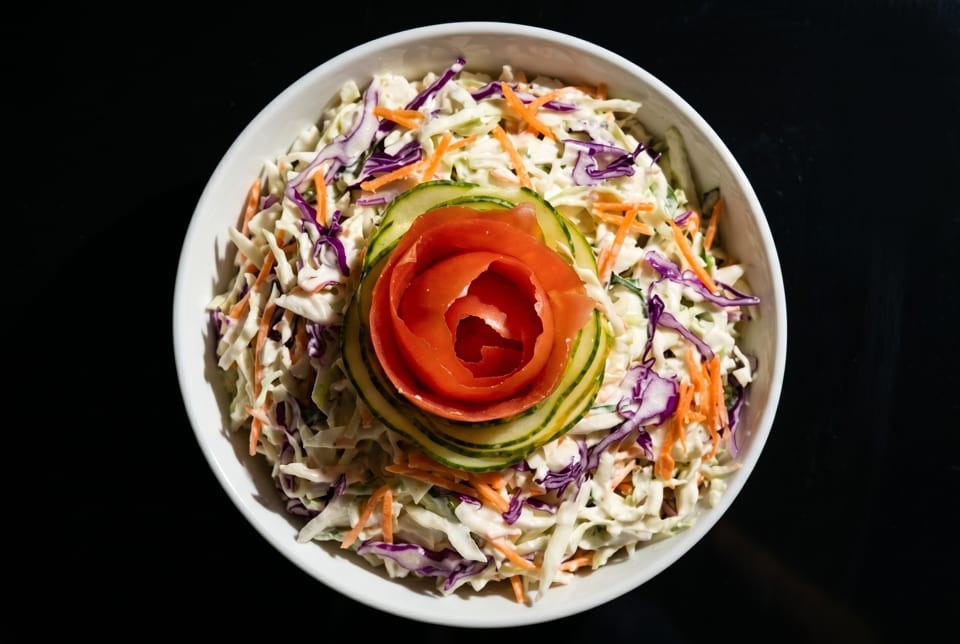 Coleslaw with shredded cabbage, carrots, and purple cabbage, garnished with a tomato and cucumber rose.