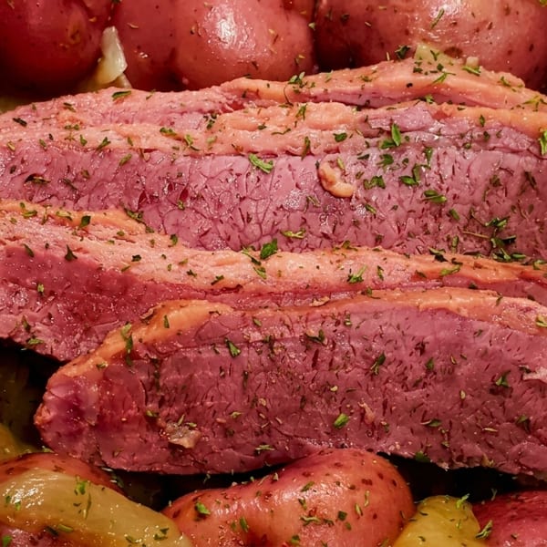 Sliced corned beef with red potatoes and cabbage, garnished with herbs.