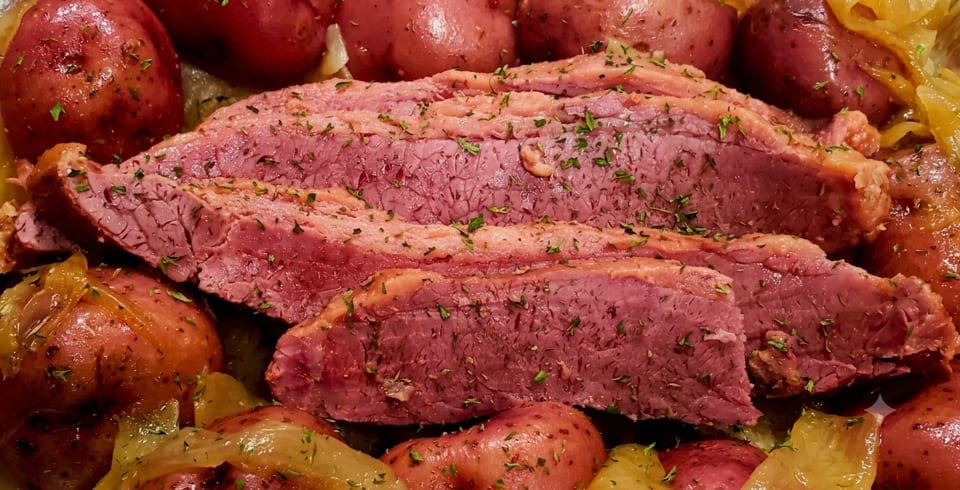 Sliced corned beef with red potatoes and cabbage, garnished with herbs.