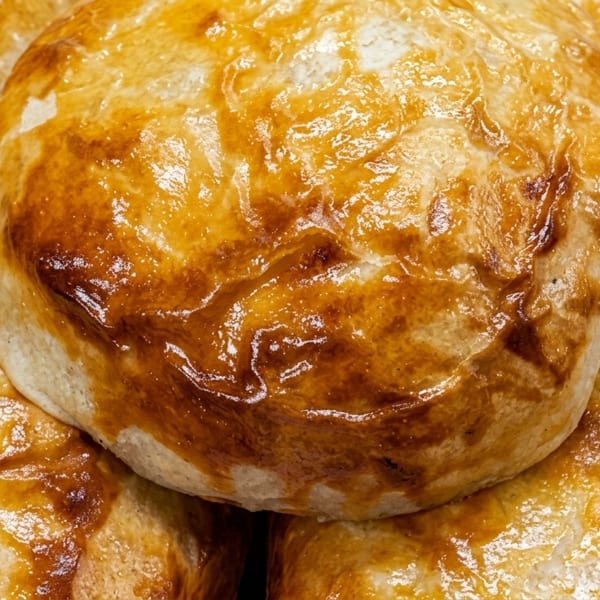 Close-up of golden-brown baked pastries, possibly empanadas or buns, on a wooden surface.