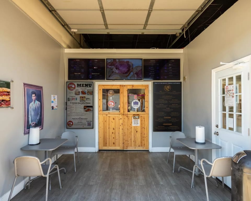 Small restaurant interior with two tables, menu boards, and wooden double doors.
