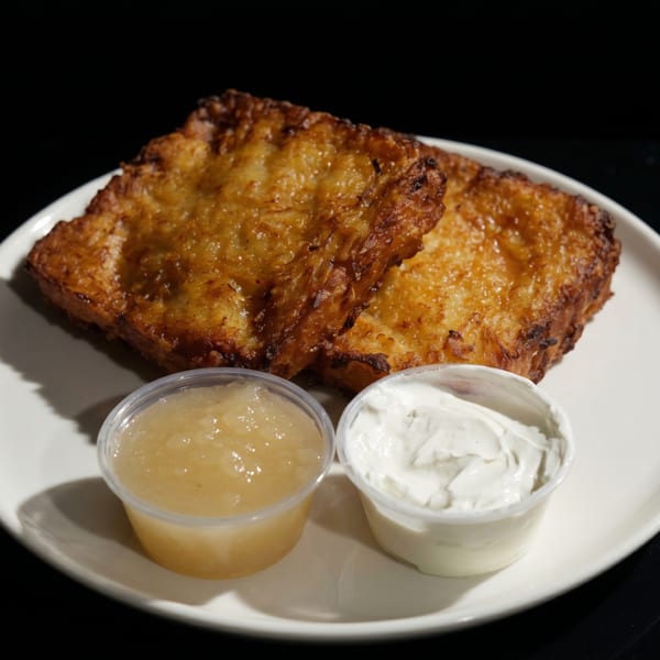 Two golden-brown potato pancakes with sides of applesauce and sour cream on a white plate.