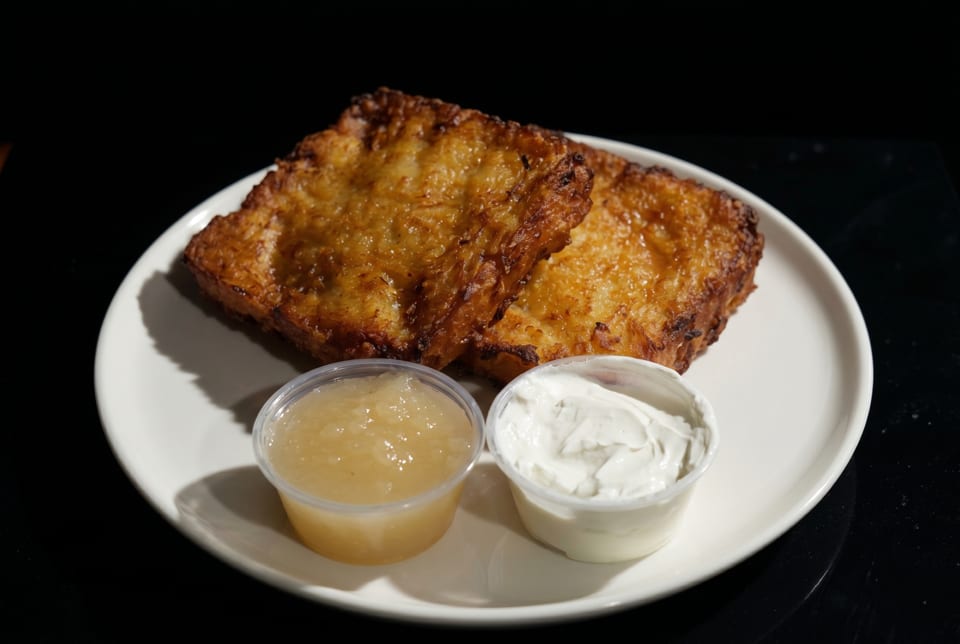 Two golden-brown potato pancakes with sides of applesauce and sour cream on a white plate.